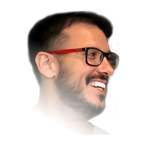 A smiling Marcus Rodrigues wearing red-framed glasses, with a beard and short hair, looking to the side.